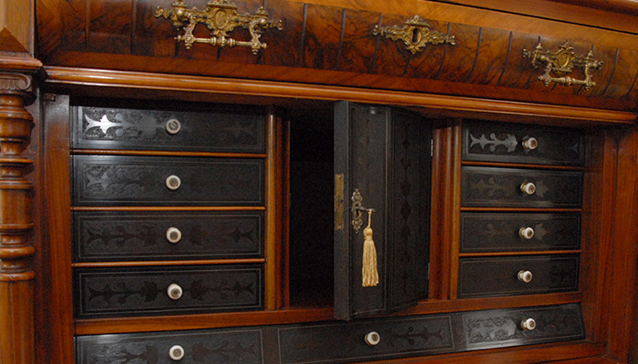 The fitted interior of a Victorian burr walnut collector's cabinet, with ebonised drawers and a central tasselled door.