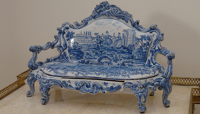 A blue and white faience settle moulded with rococo scrollwork and painted with a pastoral landscape.