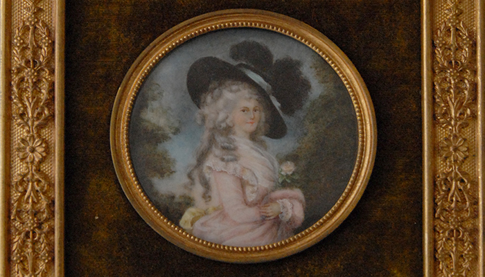 A portrait miniature of a lady in a pink gown and black plumed hat, in a gilt frame.
